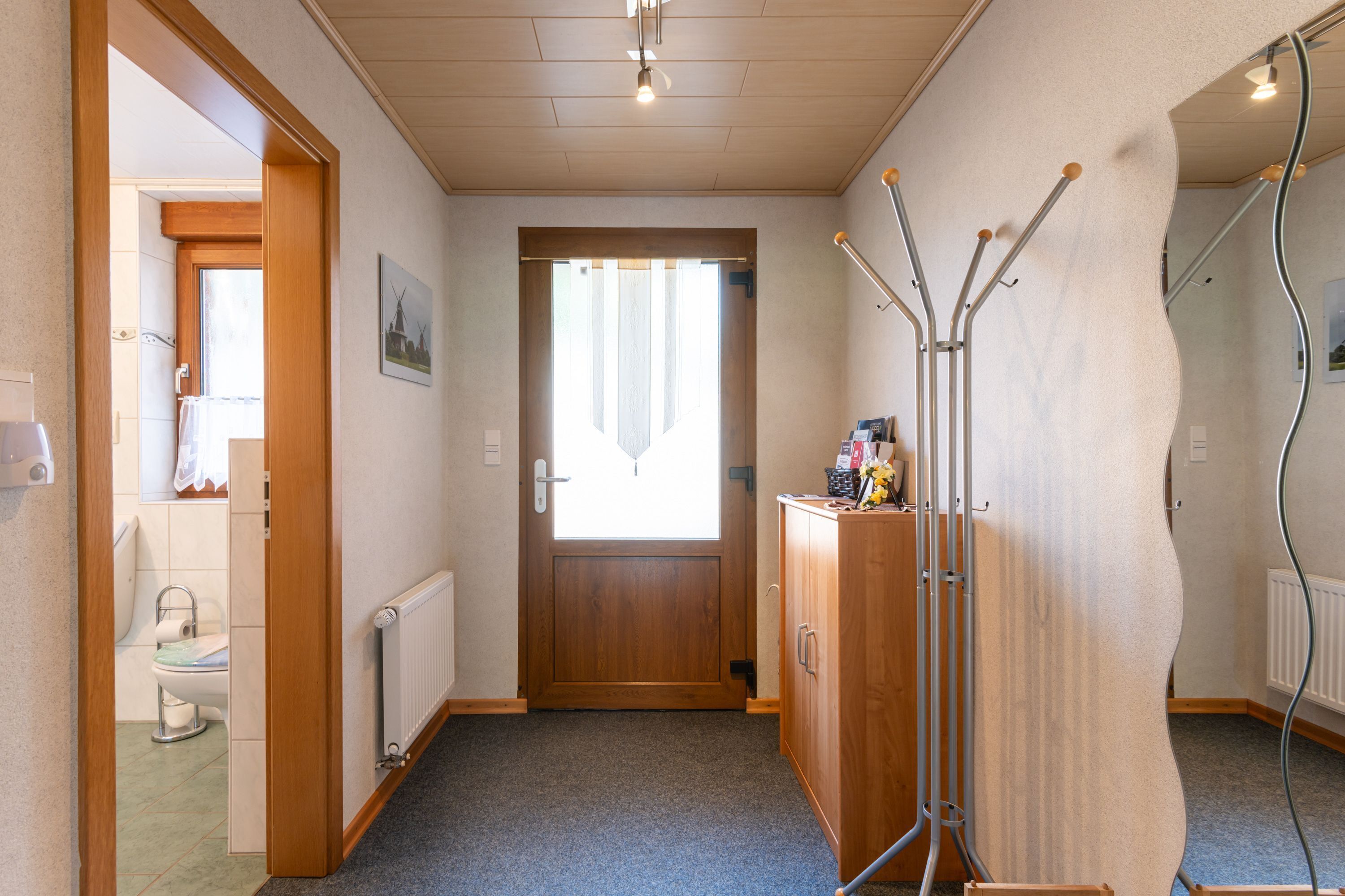 Ein Flur mit Holztür, Heizkörper und einem Schrank mit Spiegel.