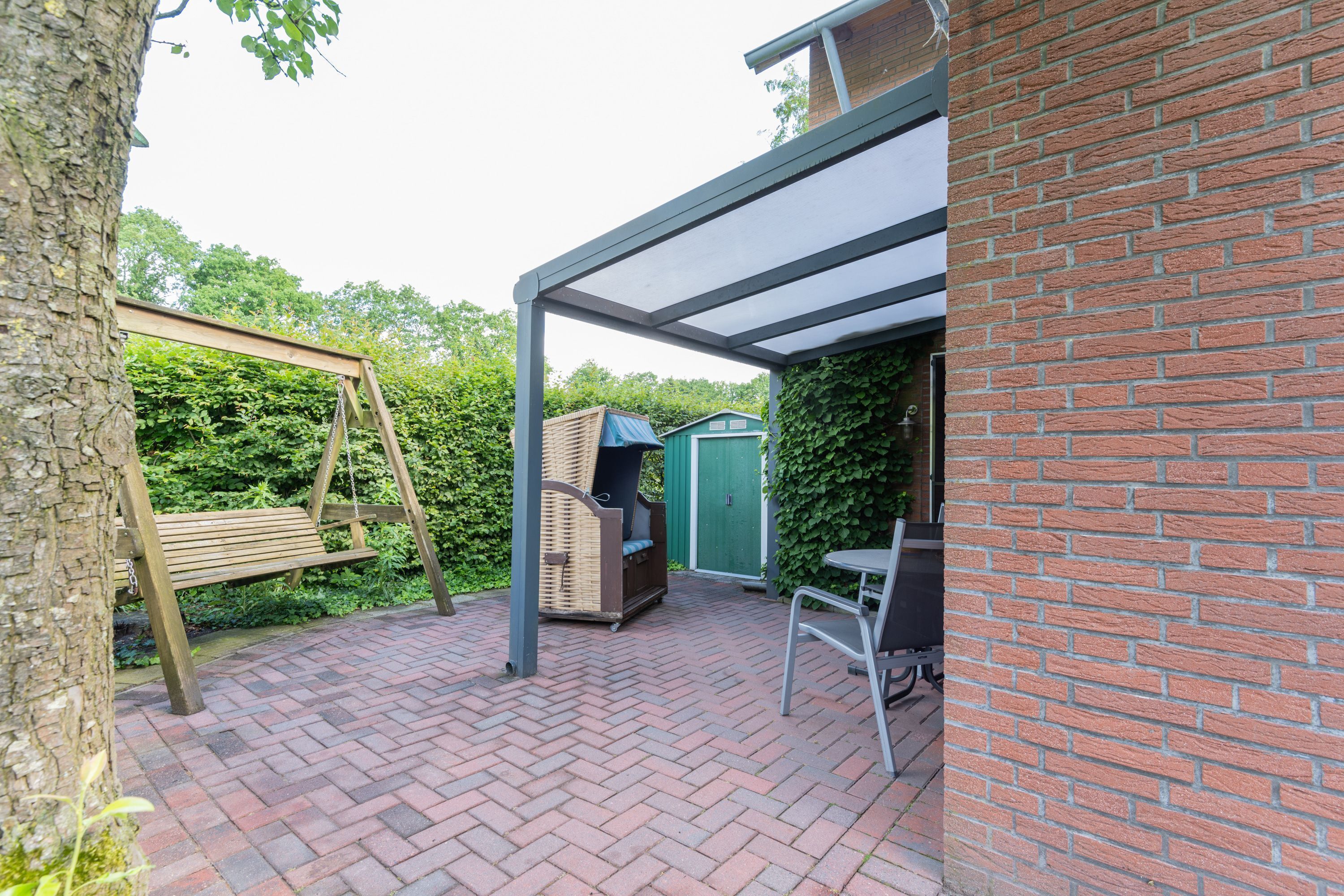 Une terrasse avec une balançoire, un barbecue et un espace salon abrité.