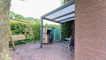 Une terrasse avec une balançoire, un barbecue et un espace salon abrité.