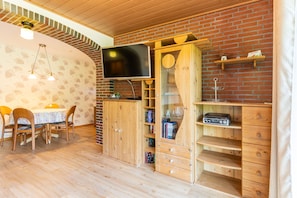 A cozy room with a brick wall, wooden furniture, a flat-screen TV, and a dining area with a table and chairs.