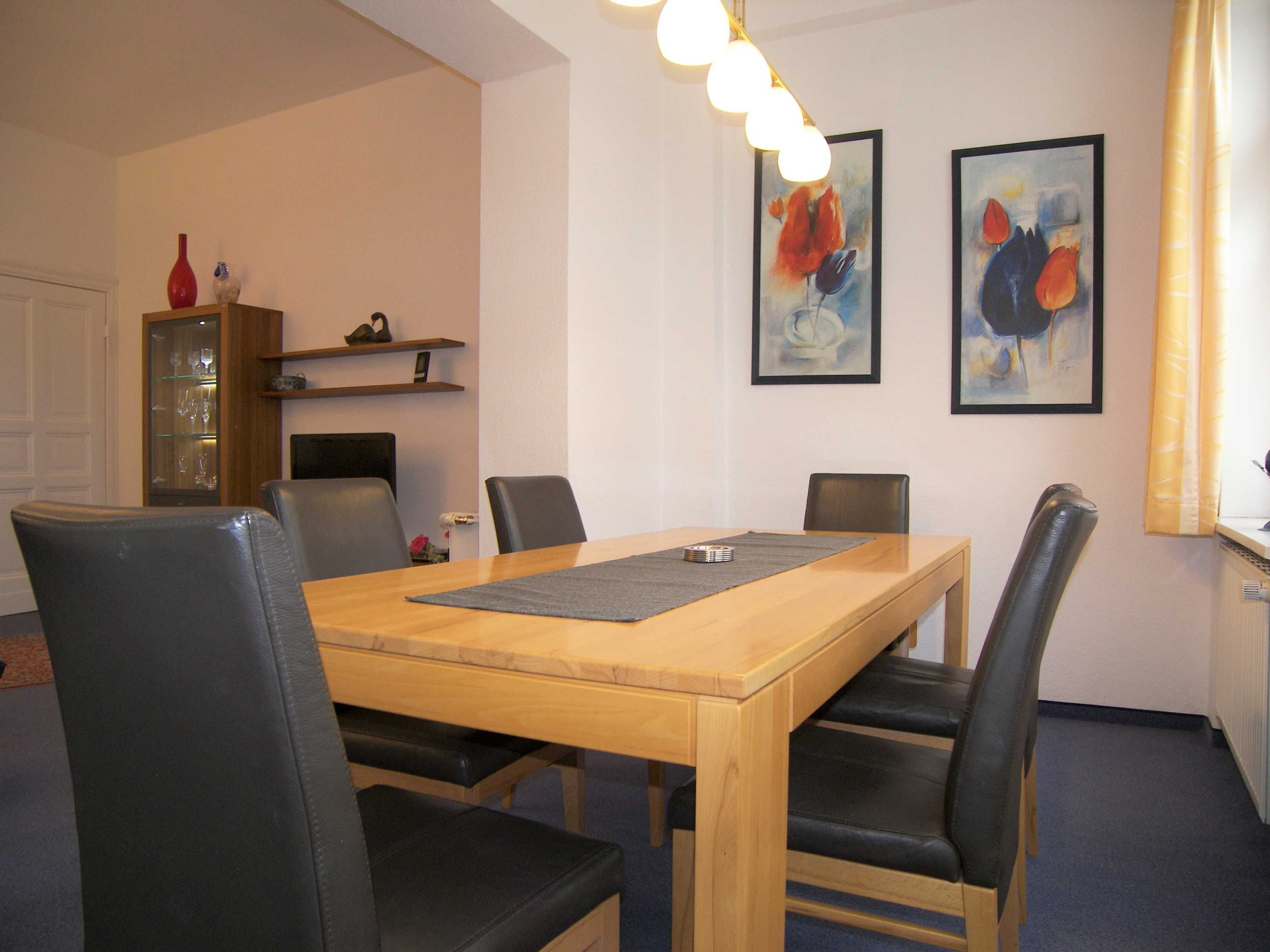 A dining area with a wooden table, black chairs, and two framed paintings on the wall.