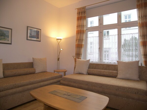 A living room with two sofas, a coffee table, a floor lamp, and a window with curtains.