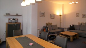 Ein modernes Wohnzimmer mit einem Holzesstisch, zwei Sofas und einem Couchtisch. Es gibt Deckenleuchten und Bilderrahmen, die an der Wand befestigt sind.
