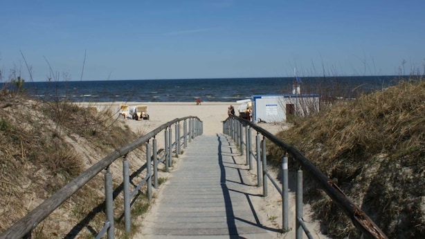 Ein Holzsteg führt zum Strand mit freiem Blick auf das Meer.