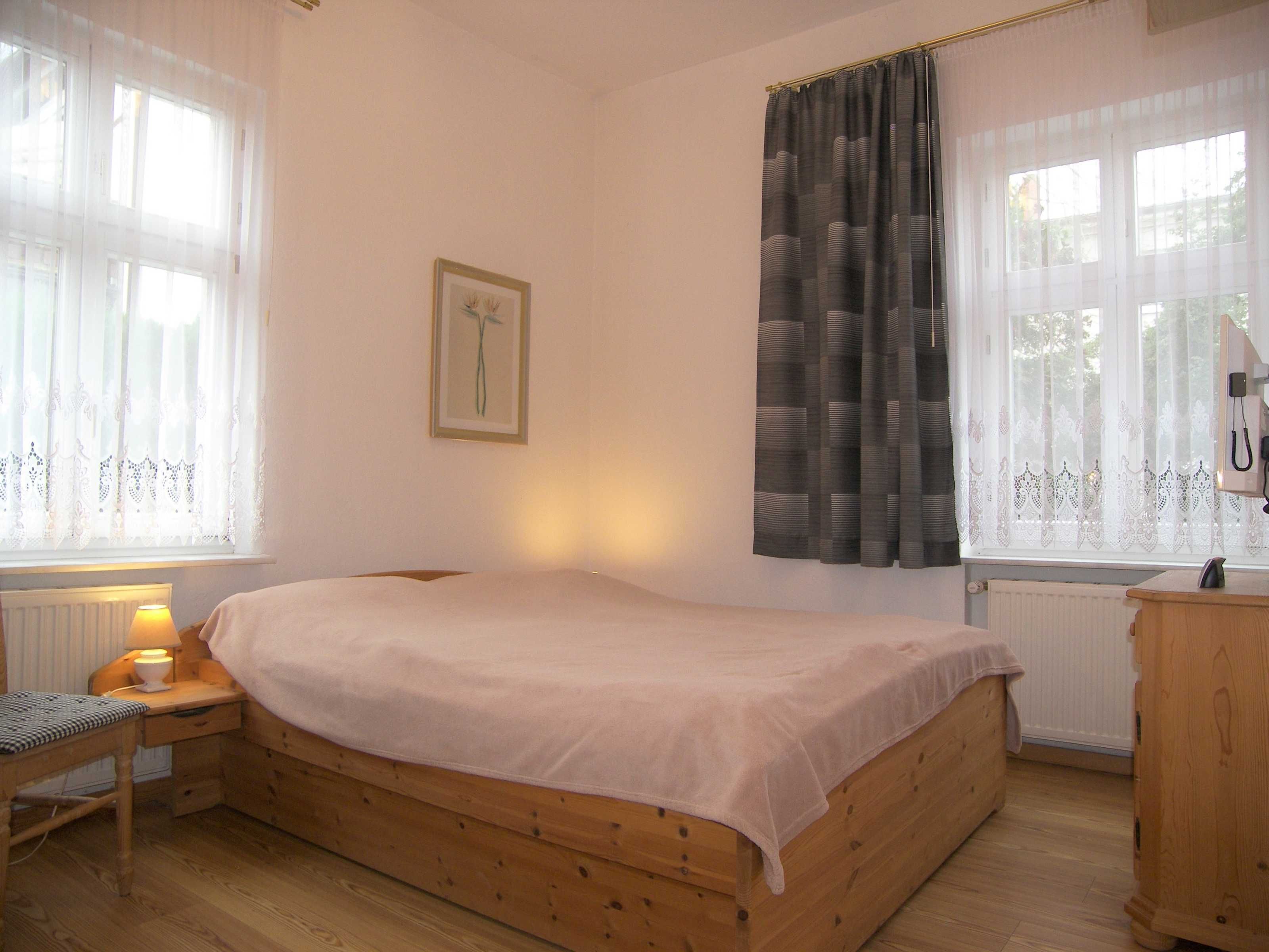 Une chambre avec un lit simple, une table de chevet avec une lampe, une commode en bois et un tableau encadré au mur.