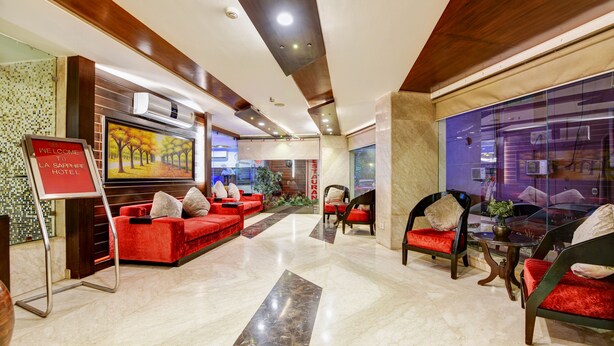 A hotel lobby with red sofas, a glass wall, and a sign that reads 'WE COME TO LA SAPPHIRE HOTEL.' - La-Sapphire Hotel (New Delhi)