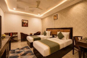 A hotel room with two beds, a desk, a chair, a ceiling fan, and a patterned rug. - La-Sapphire Hotel (New Delhi)