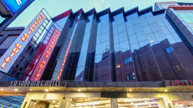 Exterior del hotel La Sapphire, con fachada de vidrio reflectante y señalización iluminada.