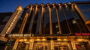 Fachada de hotel con letreros iluminados, una entrada imponente y un interior visible con asientos.
