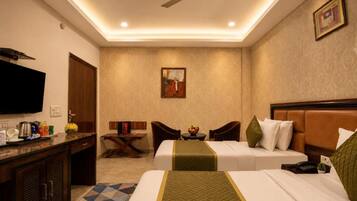 A hotel room with a bed, a desk with a flat-screen TV, a ceiling fan, and a small table with a bowl of fruit.