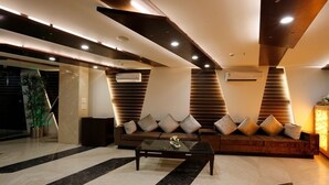 A modern lobby with a sofa, a coffee table, and a reception desk. - La-Sapphire Hotel (New Delhi)