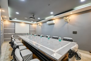 A conference room with a long table, chairs, a projector screen, and an air conditioning unit.