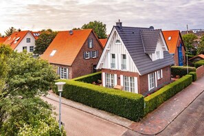 Traditional two-story house with a steeply pitched roof and red and white brickwork, set amidst well-mainters hedges and a paved driveway.
