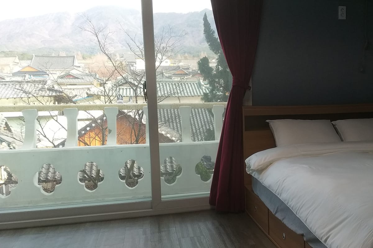 A bedroom with a large window, a bed, and a view of traditional buildings.