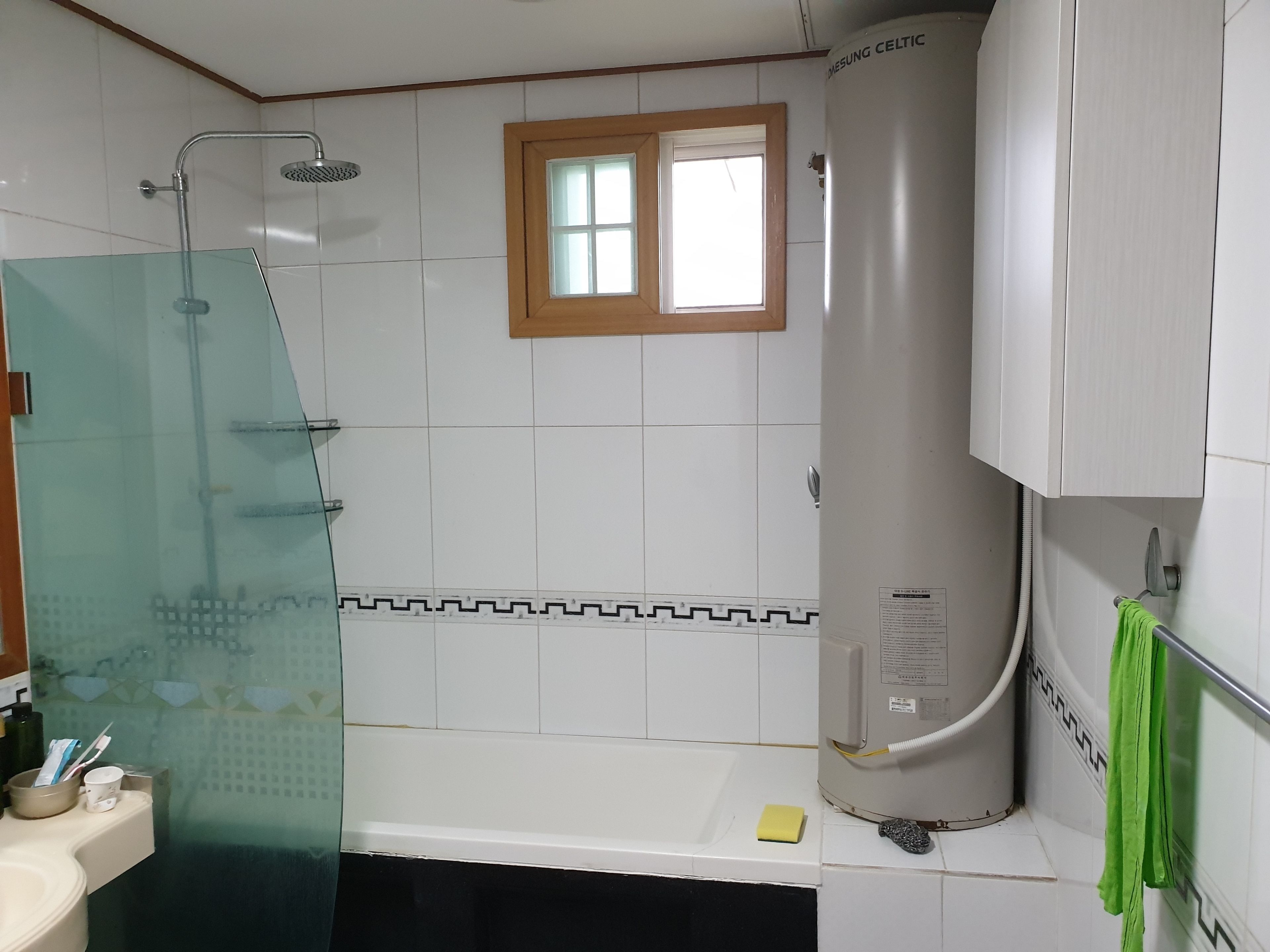 Une salle de bain avec une douche à parois de verre, une baignoire blanche, une fenêtre et un chauffe-eau.