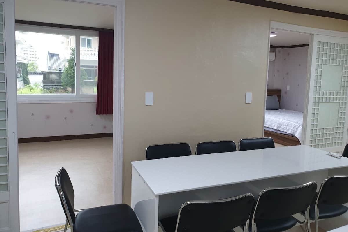 A conference room with a white table and six black chairs, a window with a red curtain, and a view of buildings outside.