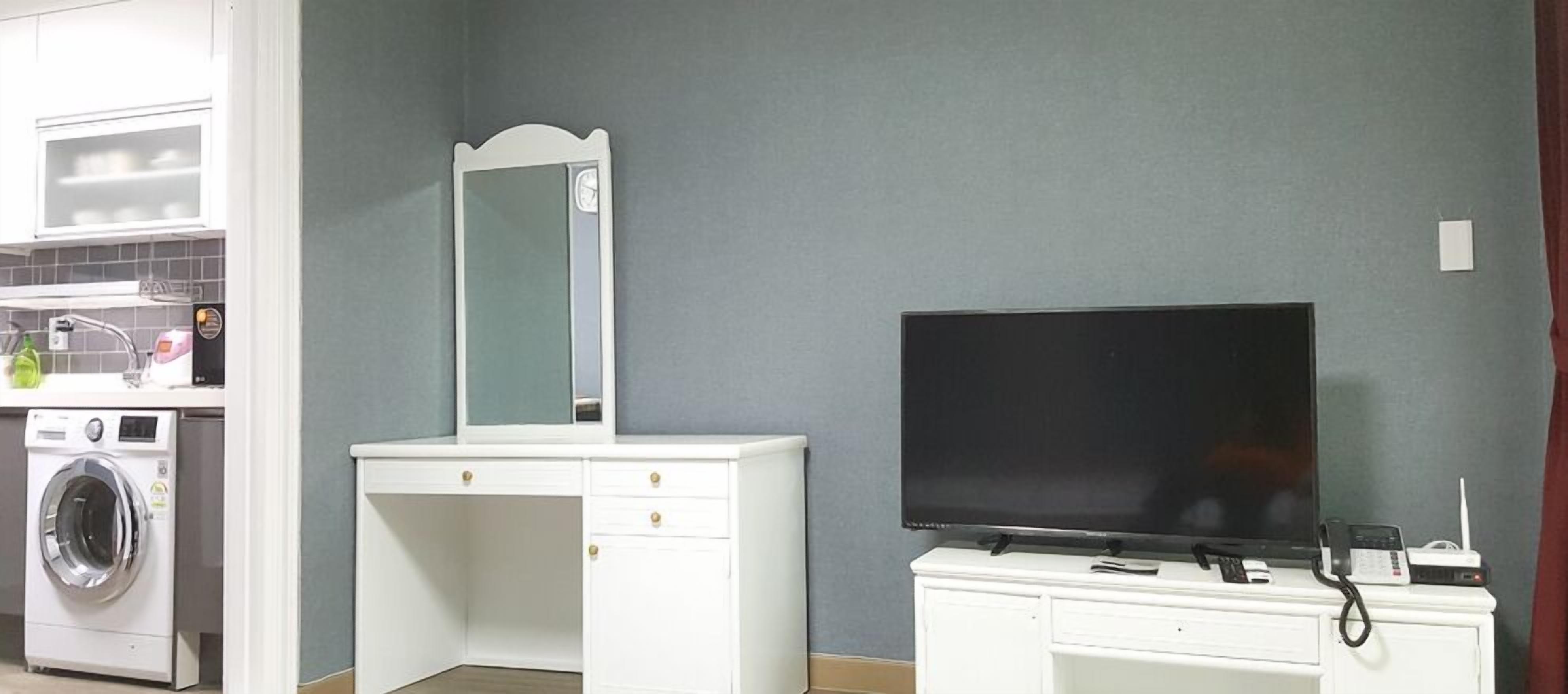 A room with a washing machine, a mirror, a television, and a phone on a cabinet.