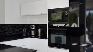 Une cuisine moderne avec des meubles blancs, un plan de travail noir, un four encastré, un four à micro-ondes et un réfrigérateur.