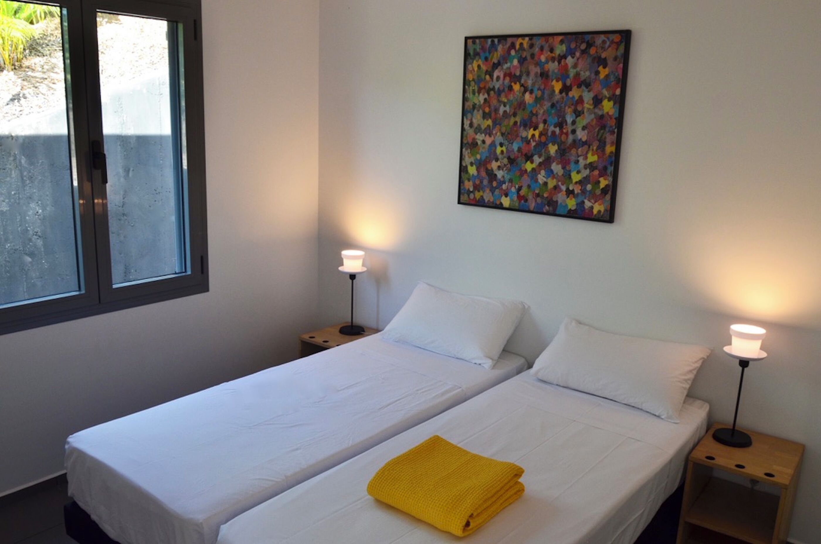 Une chambre avec deux lits simples, une fenêtre, un tableau abstrait accroché au mur et des lampes de chevet.