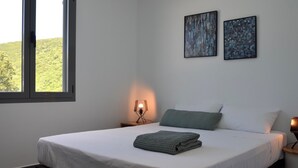 Une chambre à coucher avec un lit, deux tableaux accrochés au mur, une fenêtre et une lampe de chevet.