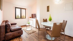 Un salon moderne avec un canapé en cuir marron, une table à manger en verre et quatre chaises, une petite table d’appoint blanche et une plante en pot.