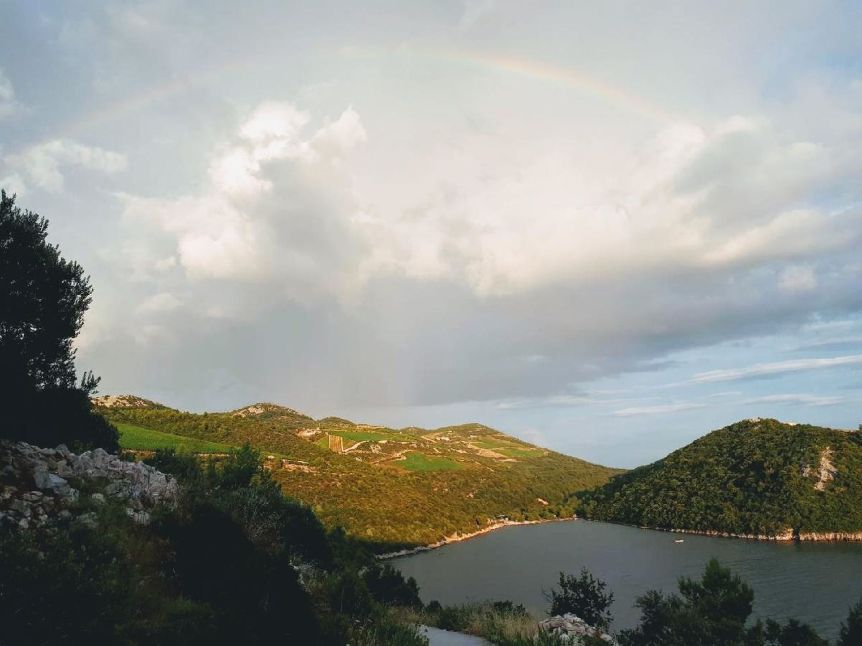 A lake surrounded by hills with a rainbow in the sky.