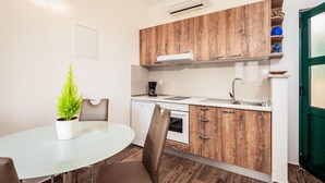 Une cuisine compacte avec des meubles en bois, un plan de travail blanc, un four encastré et un évier. Une plante en pot est posée sur la table à manger.