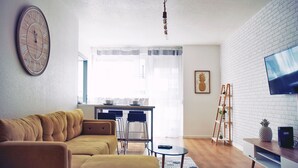 Een woonkamer met een bank, een salontafel, een televisie en een keukenhoek met een eettafel en stoelen.
