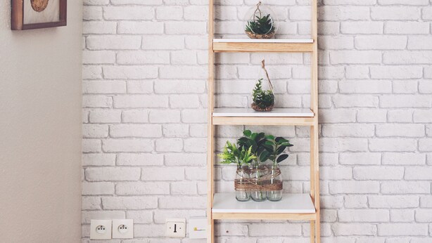 Een witte bakstenen muur met een houten vloer, een raam met een afbeelding van een ananas, en een houten plank met planten.