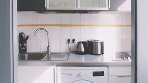 Een kleine keuken met een wasmachine, een spoelbak en een kast boven het aanrecht.