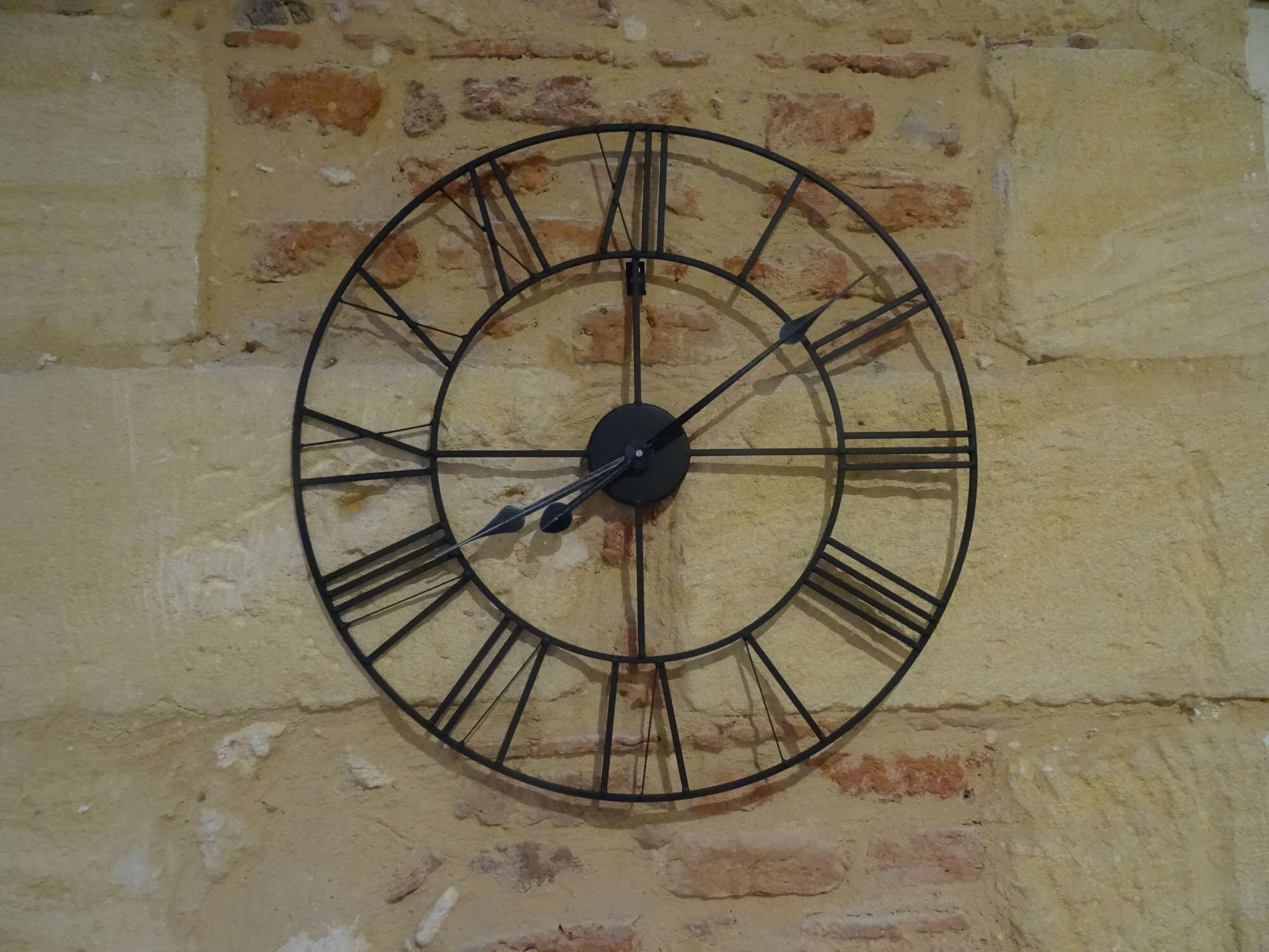 Eine runde Wanduhr mit römischen Ziffern an einer strukturierten Ziegelwand befestigt.