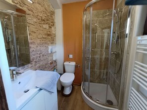 A bathroom with a stone wall, a white bathtub, a toilet, and a glass-enclosed shower. - Charming Loft "Roxane" - Habitation Saint-Clar - Historic Center - WIFI/Netflix (Bergerac)