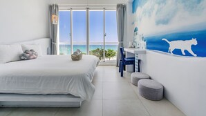 A bedroom with a large bed, a desk, and a view of the sea. - Cat at Greece (Hengchun)