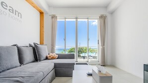 A modern living room with a grey sofa, a small table, and a view of the sea through large windows. - Cat at Greece (Hengchun)