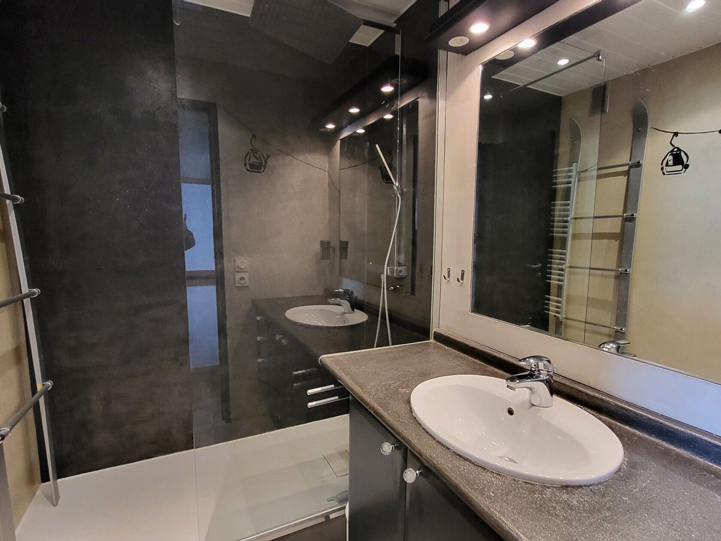 A modern bathroom with a large mirror, a sink, and a shower.