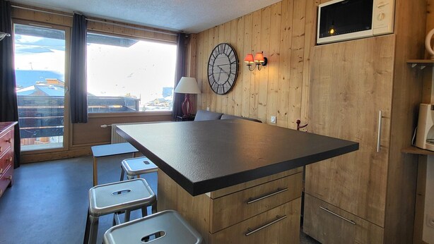 A compact kitchen with a central island, wooden cabinetry, a clock, and a window with a view of buildings. - Cozy studio with Wifi near slopes in Tignes (Tignes)