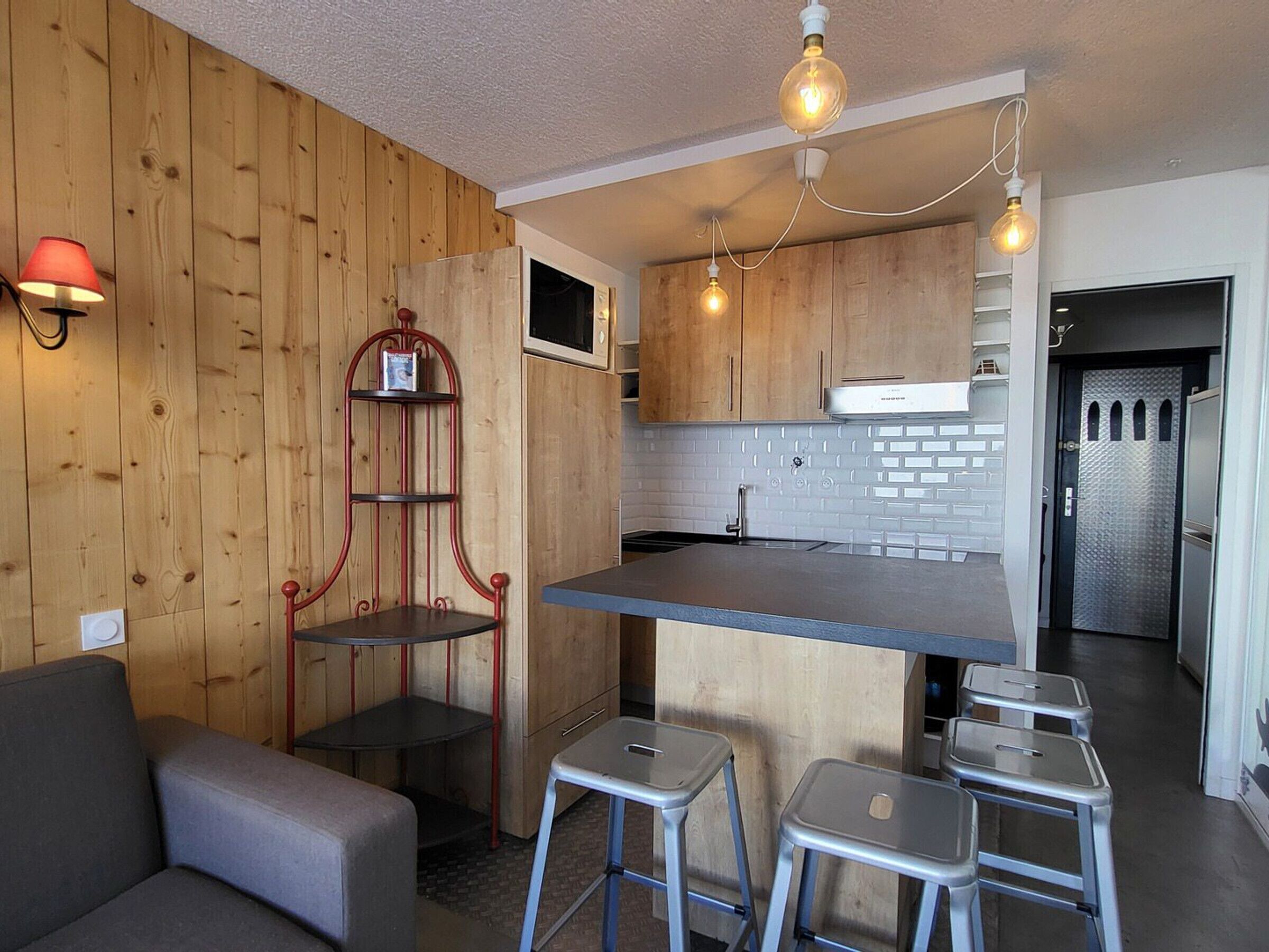 Una cocina compacta con paredes de madera, un microondas empotrado y un refrigerador de acero inoxidable.