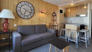 A modern living room with a grey sofa, a round wall clock, a red lamp, and a small table. - Cozy studio with Wifi near slopes in Tignes (Tignes)