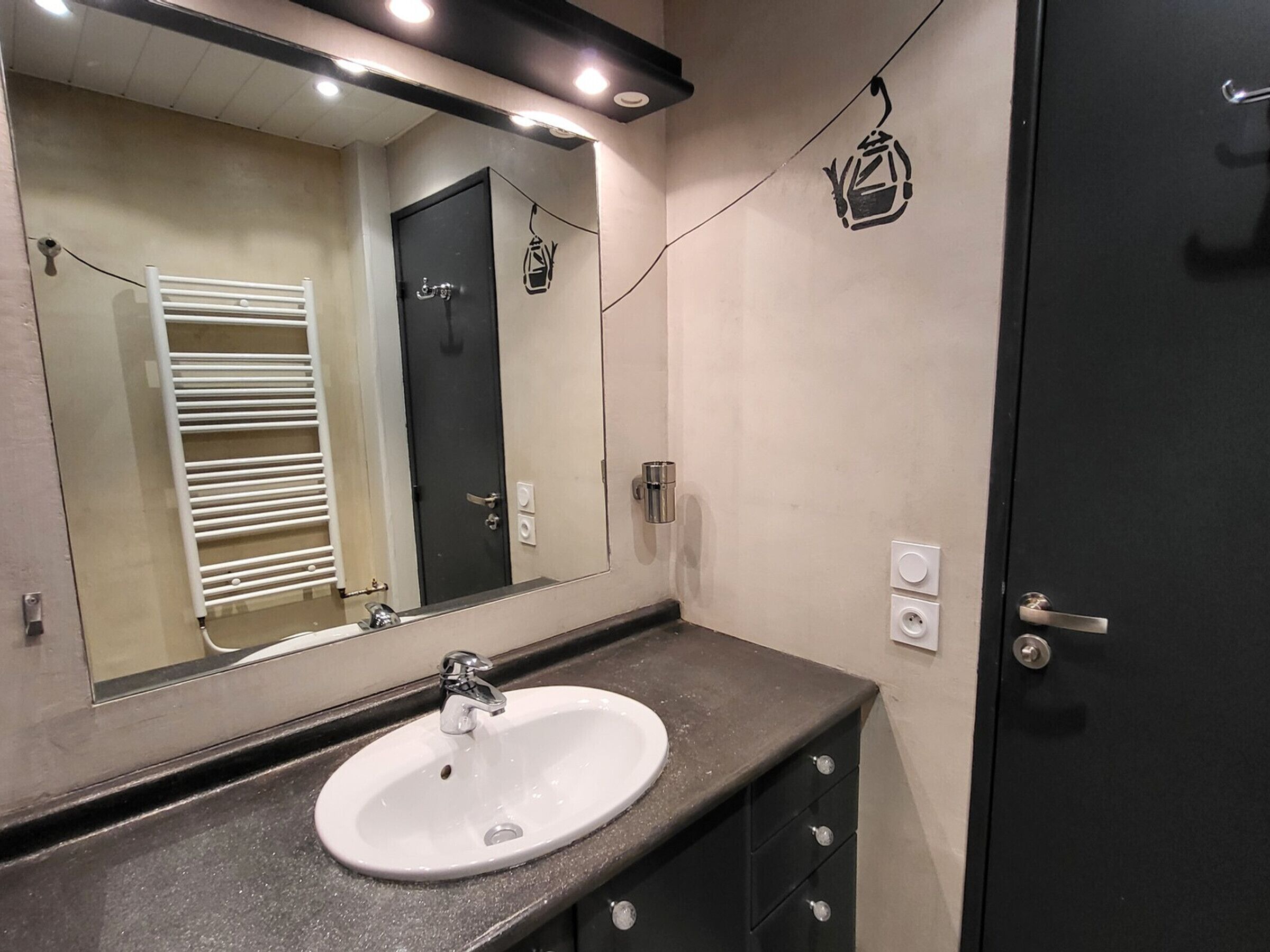 Um banheiro com pia branca, espelho, porta-toalhas e porta.