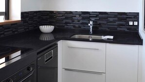 Une cuisine moderne avec des plans de travail noirs, des armoires blanches, un pare-feu noir et un évier en acier inoxydable.