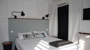 Un lit bien fait, avec des oreillers, une table de chevet, une lampe et une étagère fixée au mur, sur laquelle sont posés des livres.