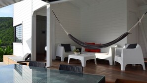 Un espace extérieur moderne, aménagé avec des sièges, un hamac, des meubles blancs et une table en verre.