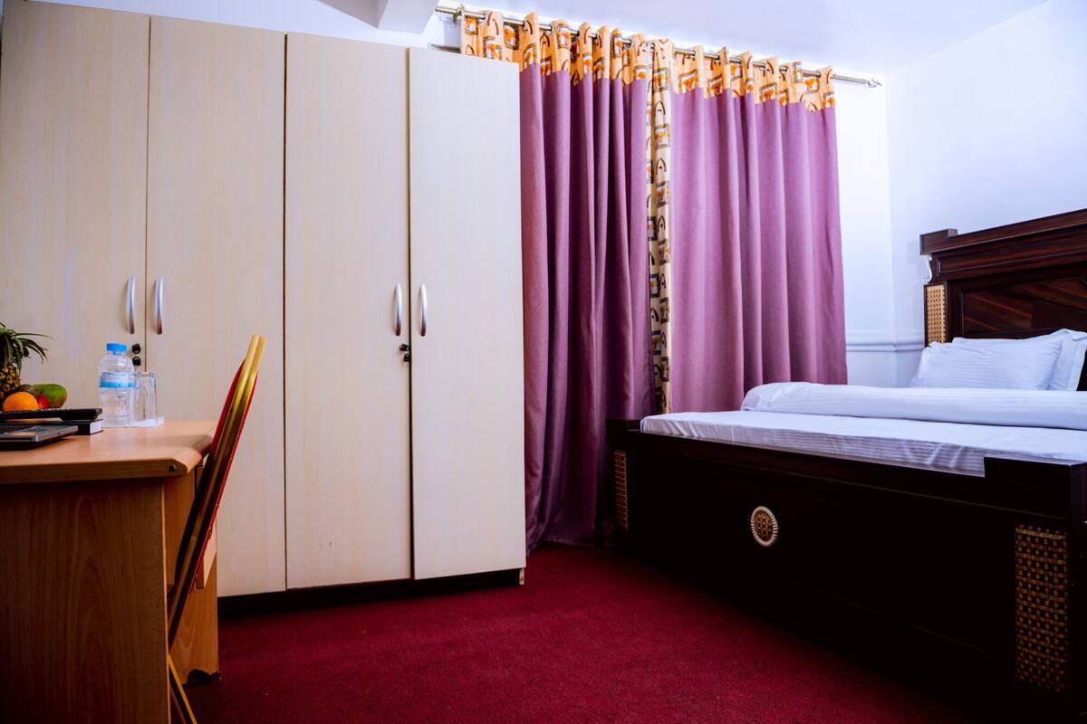 Une chambre d’hôtel comprenant un lit, un bureau avec une chaise, une armoire et une salle de bain avec un rideau de douche.