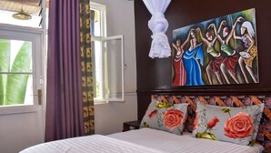 A bedroom with a bed, a window with curtains, a painting on the wall, and a headboard with floral pillows. - Zebra Boutique Hotel (Kigali)