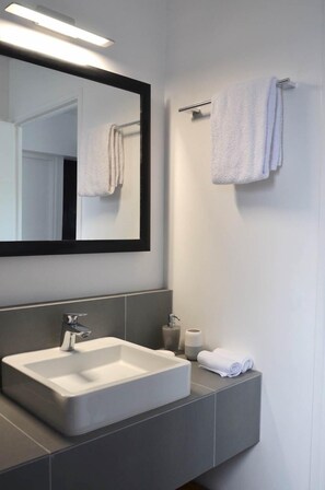 A modern bathroom with a large mirror, a white sink, and a towel rack.