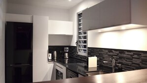 Eine moderne Küche mit einem schwarzen Kühlschrank, Edelstahlgeräten, einer schwarzen Arbeitsplatte und einer gefliesten Spritzschutzwand.