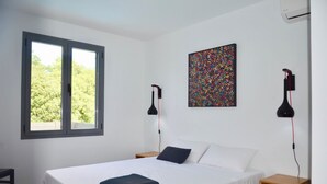 Ein Schlafzimmer mit einem Bett, einem Fenster, einem farbenfrohen abstrakten Gemälde und zwei Wandleuchten.