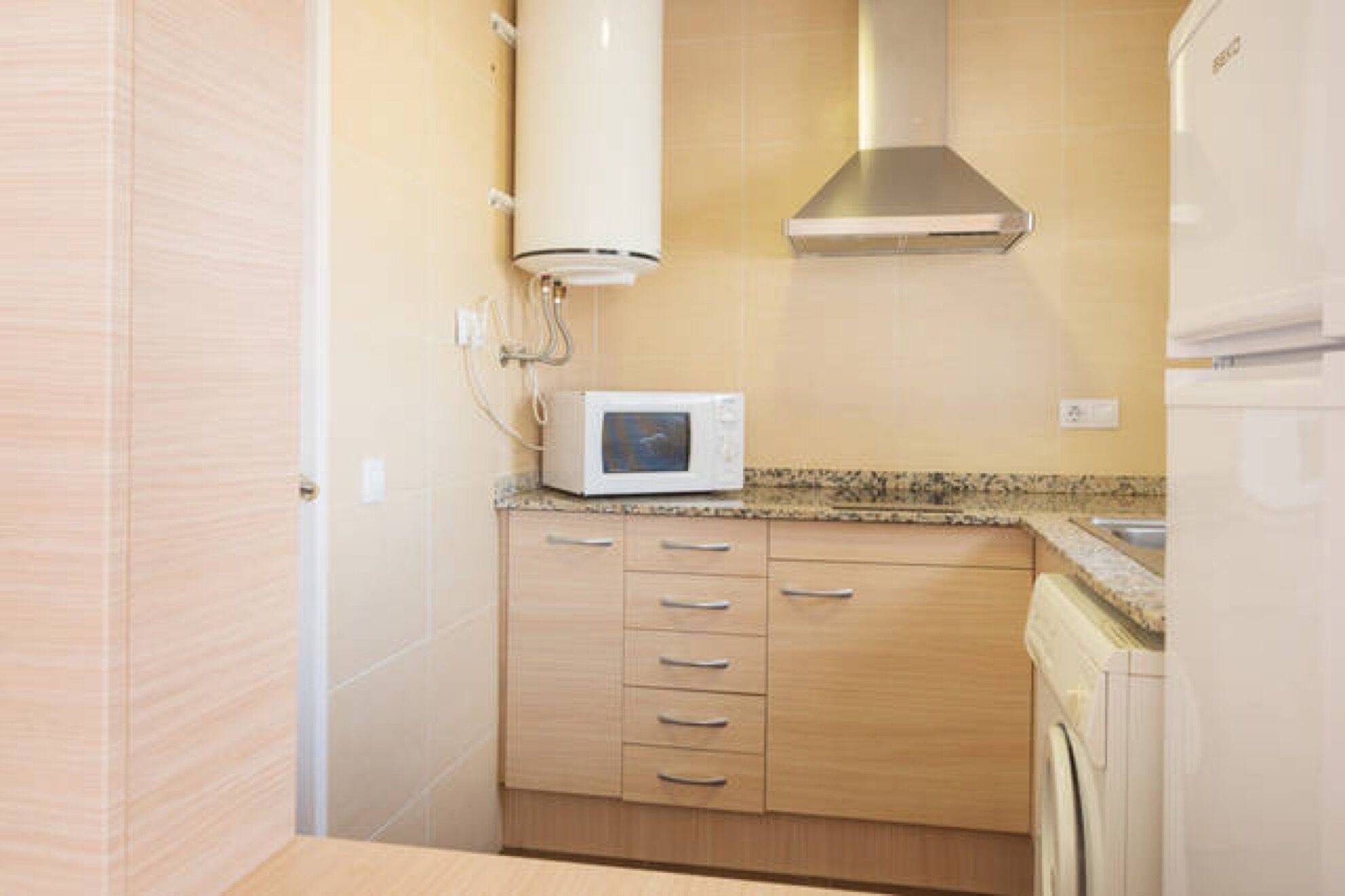 A compact kitchen with wooden cabinets, a microwave, and a stainless steel range hood.