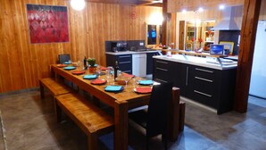 A wooden dining area with a long table set for four, a bench, and a kitchen in the background. - Chalet telegraph 13/15 people (Saint-Martin-D'arc)