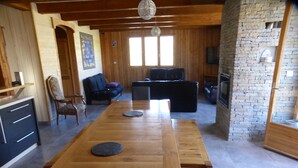 Un vaste espace de vie comprenant une longue table en bois, un canapé noir et une cheminée.